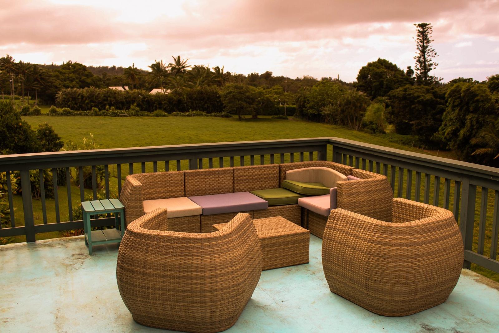 Wicker lounge chairs on the lanai at Kohala Country Haven, looking out over green pasture